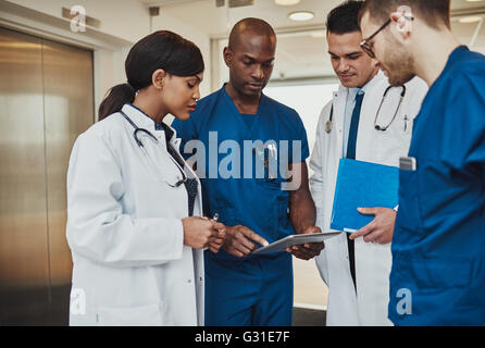 De l'équipe multiraciale doctors discussing un patient debout regroupés dans le foyer à la tablette à un ordinateur, vue en gros Banque D'Images