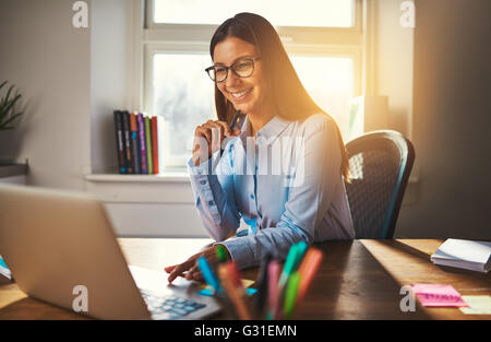 Femme travaillant à l'office à l'aide d'un ordinateur portable, les tons chauds de la lumière du soleil Banque D'Images