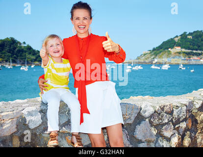 Week-end en famille. Portrait of smiling mother and daughter showing Thumbs up devant le beau paysage avec vue sur lagon avec yachts Banque D'Images