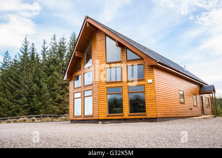 Campagne maison en bois moderne avec façade avec grandes fenêtres en verre. sapins forêt en arrière-plan. Banque D'Images