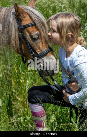 Petite fille de 6 ans avec son poney dans un pré d'été, caressée de poney d'enfant, caressant Banque D'Images