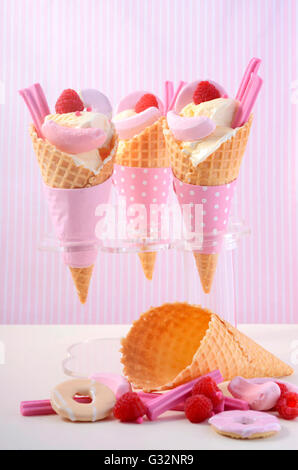 L'été est ici la vanille à thème des glaces en cônes gaufrette avec candy rose décorations sur une table en bois blanc contre une bande rose Banque D'Images