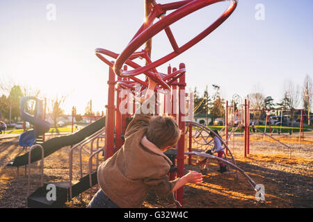 Vue arrière du garçon ça balance sur monkey bars in playground Banque D'Images