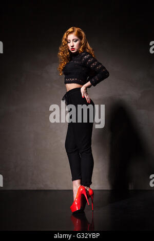 Red-haired woman posing contre du mur noir à la lumière Banque D'Images