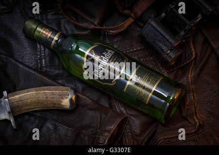 Bouteille de Glenfiddich allongé sur une veste en cuir à côté de jumelles et couteau de chasse. Banque D'Images