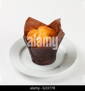 Délicieux gâteau muffin en papier brun sur la plaque sur fond blanc. Close up Vue de côté. Banque D'Images