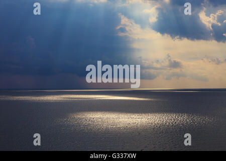 Seascape nuageux après la tempête de soleil naturels au coucher du soleil. Les rayons du soleil brillant à travers les nuages et se reflètent dans le noir se Banque D'Images