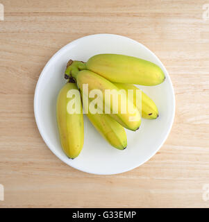 Vue de dessus d'une plaque blanche avec petites bananes sur une table en bois. Banque D'Images