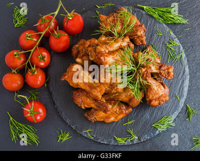 Des ailes de poulet cuit avec de la sauce barbecue sur fond noir en noir. Banque D'Images