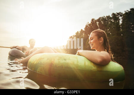 Jeune femme flottant dans une chambre à coucher de soleil sur un lac avec l'homme dans l'arrière-plan. Couple leur maison de vacances au bord du lac. Banque D'Images