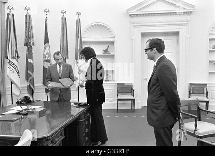 Elvis Presley présente une photographie autographiée de président américain Richard M. Nixon en tant que membre du personnel de la Maison Blanche Egil Krogh regarde sur dans le bureau ovale à la Maison Blanche le 21 décembre 1970 à Washington, DC. La réunion a été ouverte par Presley, Nixon qui a écrit une lettre de six pages en vue d'une visite avec le président et en suggérant qu'il soit fait un 'agent fédéral-at-large' dans le bureau des narcotiques et des drogues dangereuses. Banque D'Images