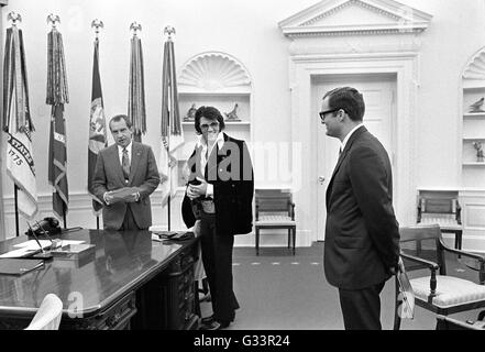 Elvis Presley présente une photographie autographiée de président américain Richard M. Nixon en tant que membre du personnel de la Maison Blanche Egil Krogh regarde sur dans le bureau ovale à la Maison Blanche le 21 décembre 1970 à Washington, DC. La réunion a été ouverte par Presley, Nixon qui a écrit une lettre de six pages en vue d'une visite avec le président et en suggérant qu'il soit fait un 'agent fédéral-at-large' dans le bureau des narcotiques et des drogues dangereuses. Banque D'Images