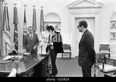 Elvis Presley présente une photographie autographiée de président américain Richard M. Nixon en tant que membre du personnel de la Maison Blanche Egil Krogh regarde sur dans le bureau ovale à la Maison Blanche le 21 décembre 1970 à Washington, DC. La réunion a été ouverte par Presley, Nixon qui a écrit une lettre de six pages en vue d'une visite avec le président et en suggérant qu'il soit fait un 'agent fédéral-at-large' dans le bureau des narcotiques et des drogues dangereuses. Banque D'Images