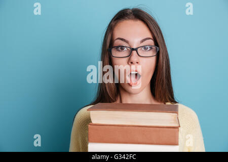 Close-up portrait of a young woman holding a surpris des livres lourds isolé sur le fond bleu Banque D'Images