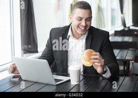 Portrait of happy smiling young business man sitting avec verre de boisson et hamburger en fast-food restaurant interior Banque D'Images