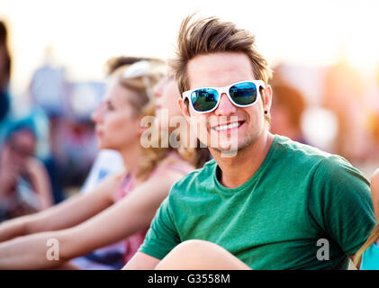 Teenage boy at summer music festival, assis sur le sol Banque D'Images