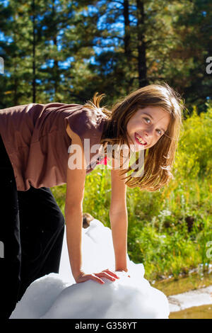 A smiling girl grimpe sur un bloc de glace sur une journée ensoleillée. Elle porte un t-shirt et un grand sourire. Banque D'Images