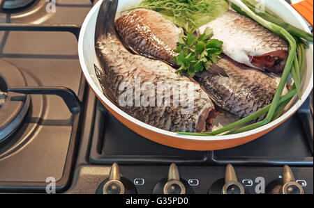 Dans une grande poêle les légumes pelés et carpe poisson : l'oignon, l'aneth, la laitue. Situé sur une cuisinière à gaz. Banque D'Images