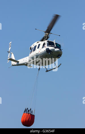 Hélicoptère avec un seau Bambi rempli d'eau pour lutter contre un incendie de forêt Banque D'Images