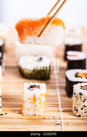 Un saumon nigiri sushi se faire prendre avec des baguettes avec différents types de sushi maki sushi en bois pièces sur un mat dans le bac Banque D'Images