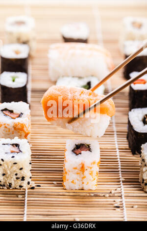 Un saumon nigiri sushi se faire prendre avec des baguettes avec différents types de sushi maki sushi en bois pièces sur un mat dans le bac Banque D'Images