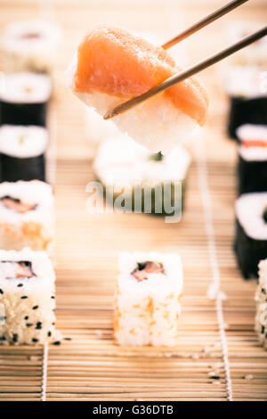 Un saumon nigiri sushi se faire prendre avec des baguettes avec différents types de sushi maki sushi en bois pièces sur un mat dans le bac Banque D'Images