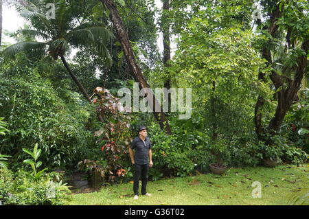 Un homme portant un chapeau est debout dans le jardin d'un hôtel de charme près de Kandy, Sri Lanka, fumer une cigarette sur un jour de mousson. Banque D'Images