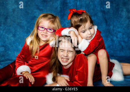 Trois sœurs, robes sont empilés sur l'autre pour un portrait de Noël devant un fond bleu. Banque D'Images