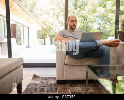 Portrait of mature homme assis sur un canapé avec vos écouteurs à l'aide d'ordinateur portable. Ambiance man working on laptop at home. Banque D'Images