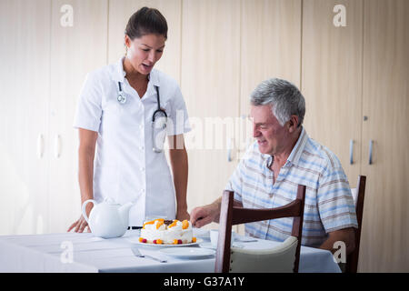 Femme médecin aînés célébration anniversaire de l'homme dans la salle de séjour Banque D'Images