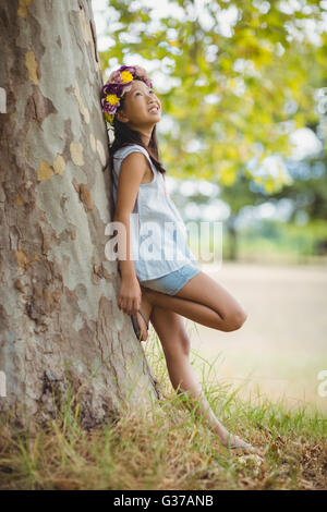Thoughtful girl leaning on tree trunk in park Banque D'Images