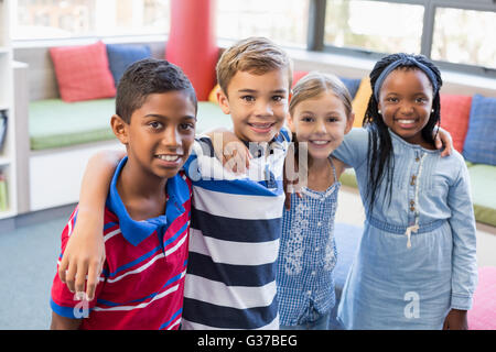 Les enfants de l'école souriant debout avec bras autour de in library Banque D'Images