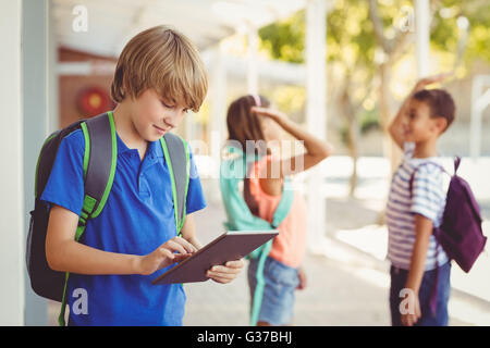 Schoolboy using digital tablet in school corridor Banque D'Images