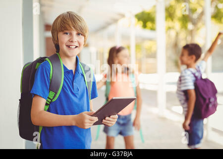 Schoolboy holding digital tablet in school corridor Banque D'Images