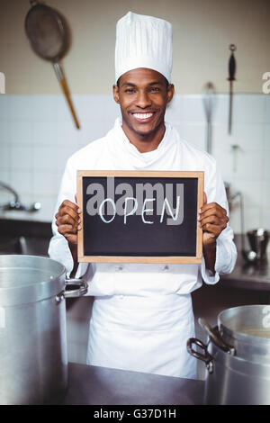 Smiling chef montrant chalkboard with open sign Banque D'Images