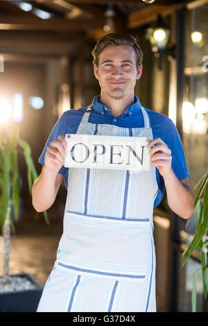 Portrait of smiling chef holding open sign Banque D'Images