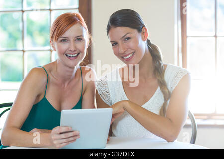 Deux smiling women sitting in restaurant avec une tablette numérique Banque D'Images
