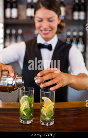 Bartender pouring un verre d'un shaker à un comptoir de bar en verre Banque D'Images