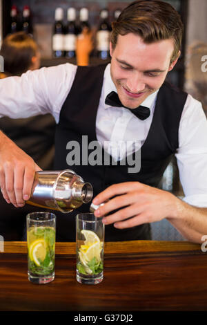 Bartender pouring un verre d'un shaker à un comptoir de bar en verre Banque D'Images