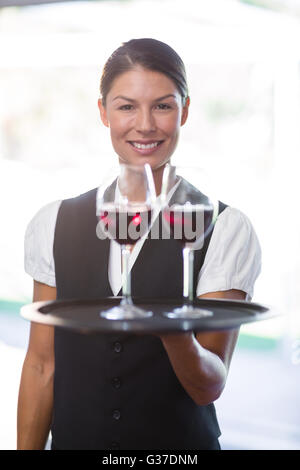 Smiling waitress holding un plateau avec des verres de vin rouge Banque D'Images