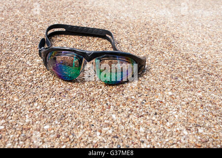 Lunettes pour nager sur un plancher de béton avec petit pierre près de la piscine. Banque D'Images