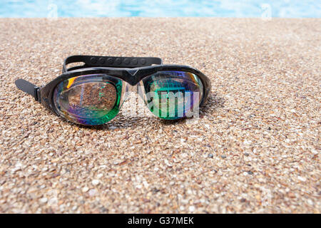 Lunettes pour nager sur un plancher de béton avec petit pierre près de la piscine. Banque D'Images