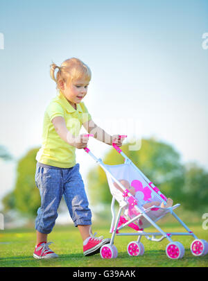 Cute little baby girl walking avec la pram en plein air, de jouets d'enfants heureux de jouer dans le parc par une belle journée ensoleillée Banque D'Images