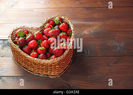 Très belle arrière-plan avec des fraises fraîches dans un panier en osier en forme de coeur en osier sur vieux fond en bois brun Banque D'Images