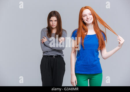 Deux smiling redhead et contrarié brunette young women standing over white background Banque D'Images