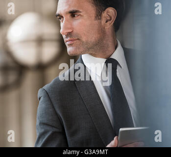 Homme d'entreprise pensive with digital tablet looking away Banque D'Images