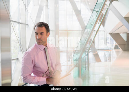 La pensive businessman looking down in modern office lobby Banque D'Images