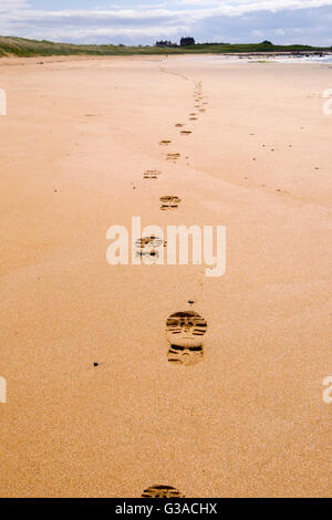 Ligne de footprints boot imprime s'éloignant dans le sable le long du chemin côtier Fife marée basse route avec walker en distance. West Beach Elie Ecosse UK Banque D'Images