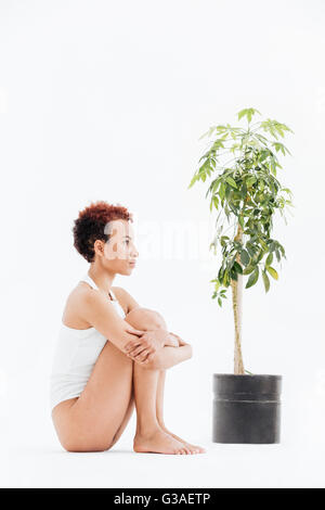 Pensive african american woman et la pensée près de petit arbre en pot sur fond blanc Banque D'Images