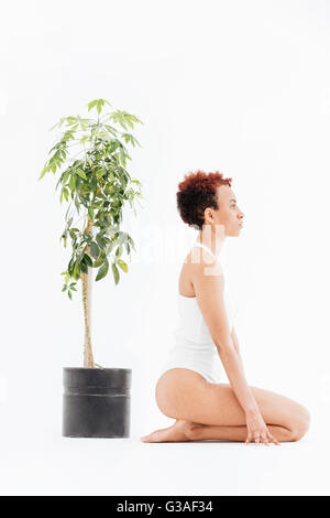 Profil de pacifiée african american woman près de petit arbre en pot sur fond blanc Banque D'Images